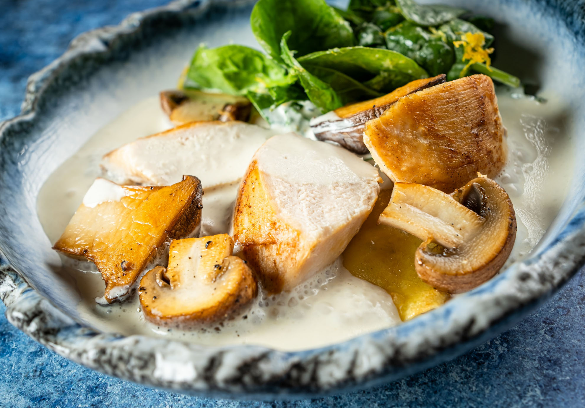 Kerámia tál krémes mártással, pirított gombaszeletekkel és csirkehúsdarabokkal, friss zöldségekkel díszítve. Az étel gazdag és csábítóan néz ki.